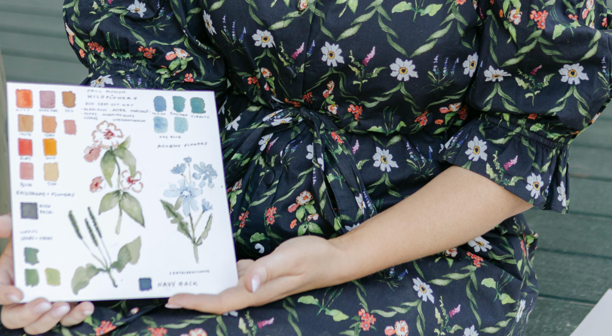 Person holding a book with illustrations of flowers and color swatches, wearing a floral dress.