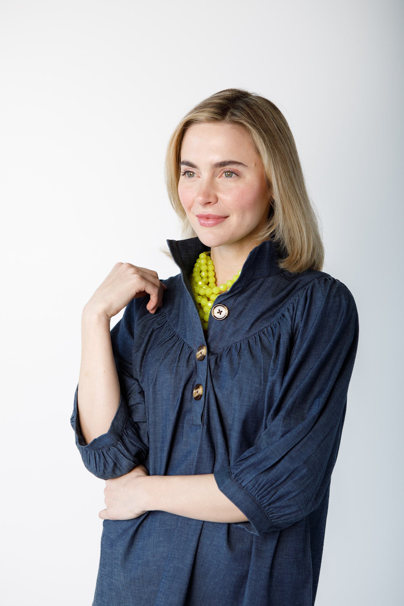 Woman wearing a blue long sleeve top with green necklace on a white background