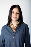 Woman wearing a long sleeve blue top with brown chunky necklace on a white background