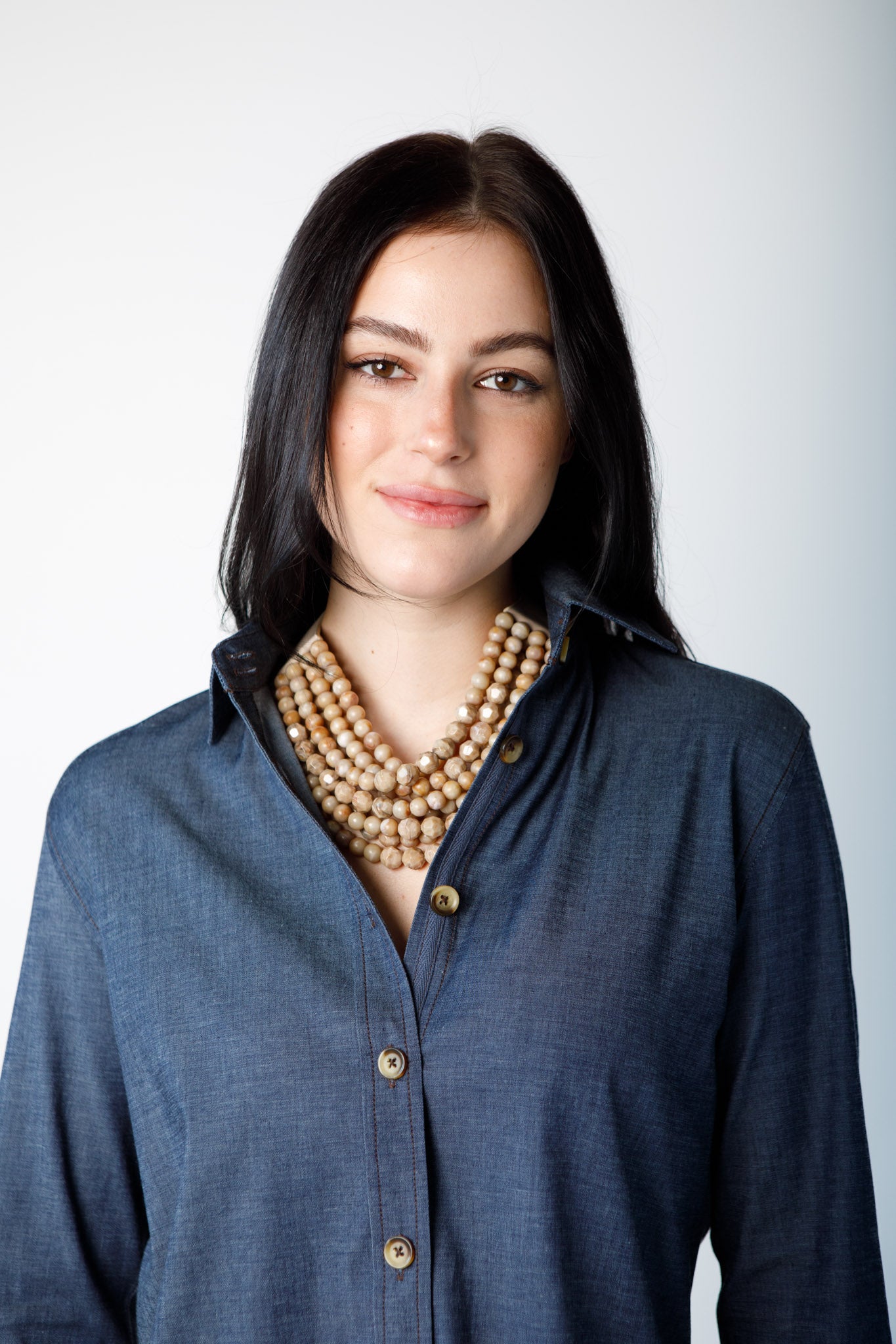 Woman wearing a long sleeve blue top with brown chunky necklace on a white background