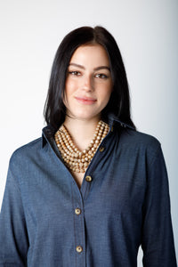 Woman wearing a long sleeve blue top with brown chunky necklace on a white background