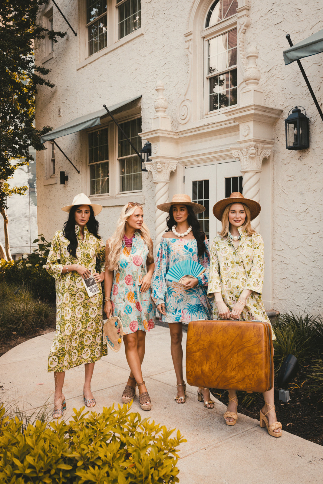 Four women in vintage-style dresses standing outside a white building.