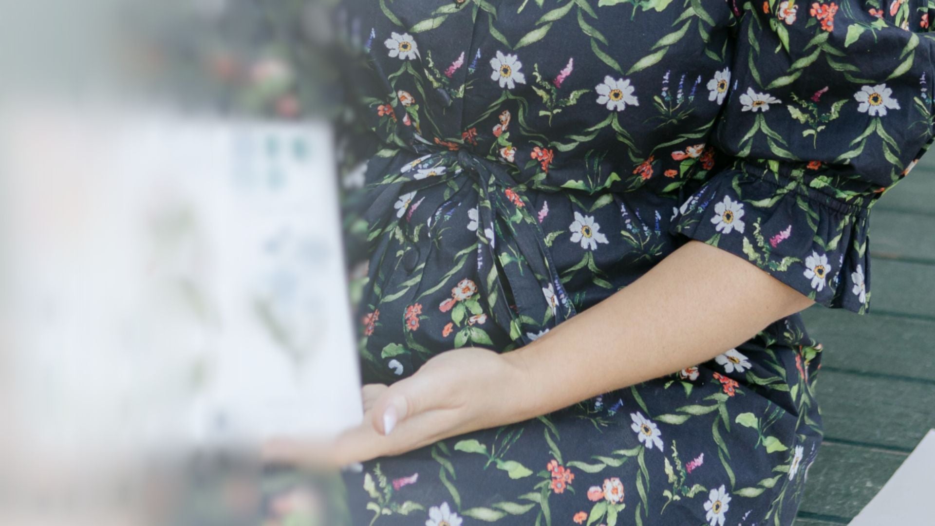Person wearing a dark floral dress sitting on a bench.